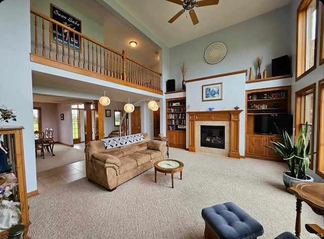 living room with high vaulted ceiling, ceiling fan, a tiled fireplace, and carpet floors