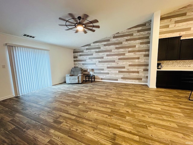 unfurnished living room featuring lofted ceiling, wood walls, ceiling fan, and light hardwood / wood-style floors