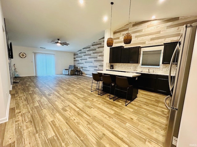 kitchen featuring light wood-type flooring, stainless steel fridge, a kitchen breakfast bar, ceiling fan, and lofted ceiling