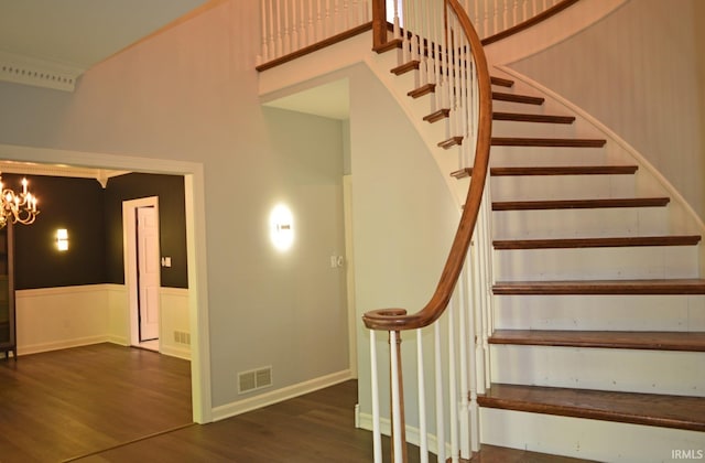 stairway with a high ceiling, wood-type flooring, and a chandelier