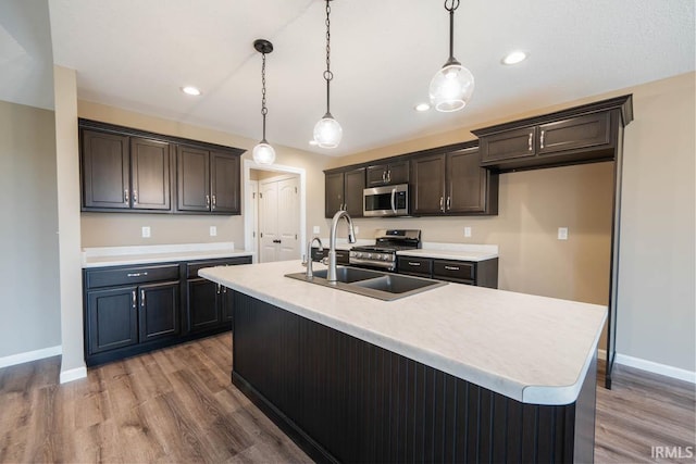 kitchen featuring an island with sink, sink, wood-type flooring, decorative light fixtures, and stainless steel appliances