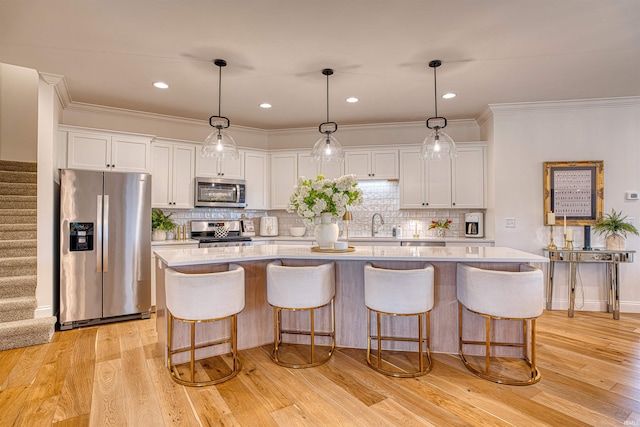 kitchen featuring light hardwood / wood-style flooring, appliances with stainless steel finishes, white cabinetry, pendant lighting, and a kitchen island