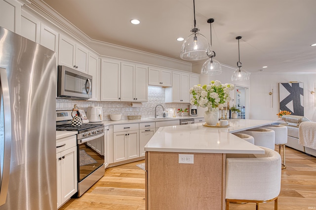 kitchen featuring a kitchen island, light hardwood / wood-style floors, stainless steel appliances, ornamental molding, and white cabinets