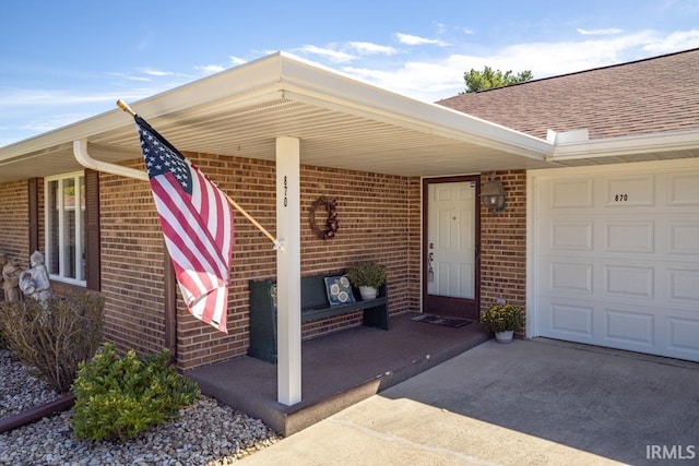 view of exterior entry featuring a garage, concrete driveway, brick siding, and roof with shingles