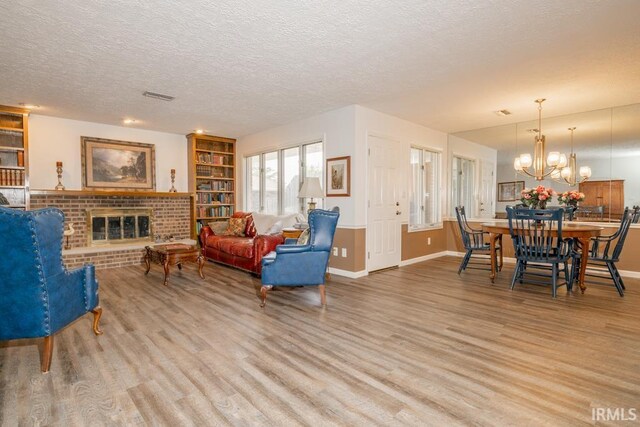 living room with a textured ceiling, light hardwood / wood-style flooring, an inviting chandelier, and a fireplace