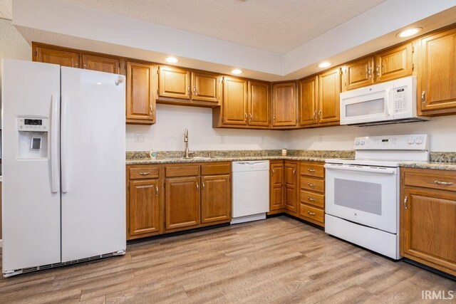 kitchen featuring light wood-type flooring, white appliances, a textured ceiling, light stone counters, and sink