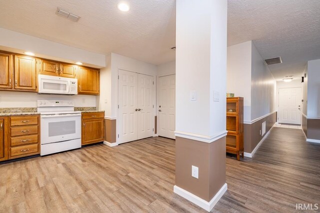 kitchen with light wood-type flooring, white appliances, and a textured ceiling