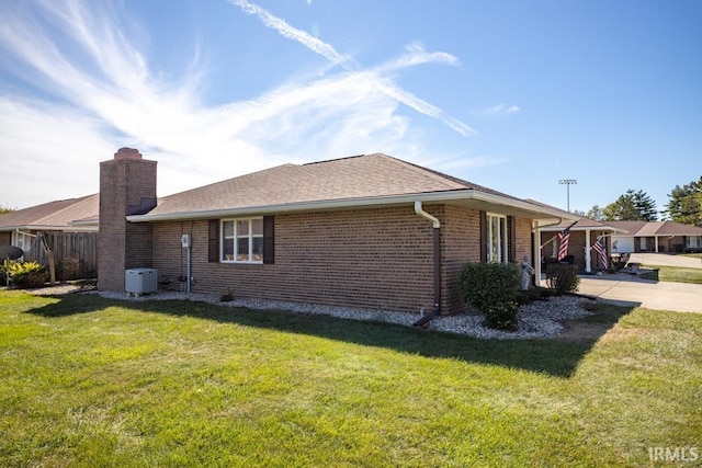 view of side of property featuring roof with shingles, a chimney, a lawn, and brick siding