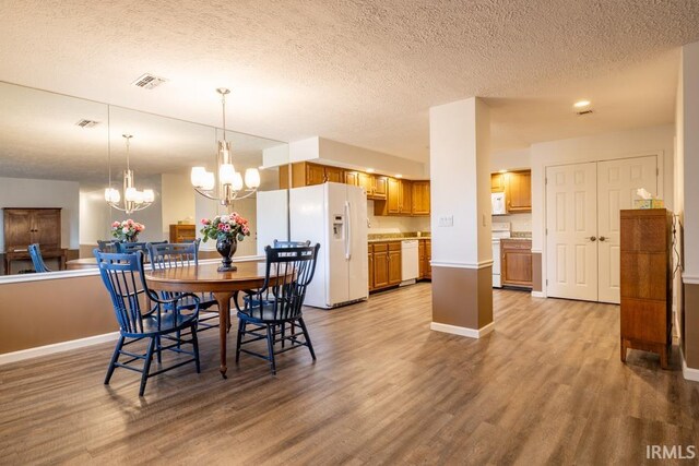 dining area with a textured ceiling, light hardwood / wood-style flooring, and an inviting chandelier