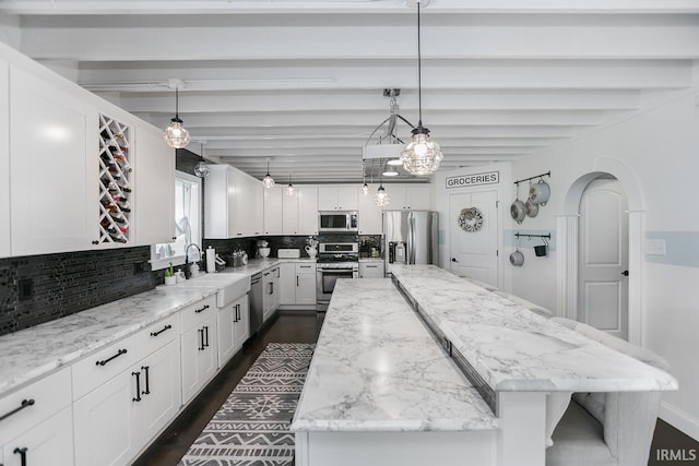 kitchen with a kitchen island, beamed ceiling, appliances with stainless steel finishes, and decorative light fixtures