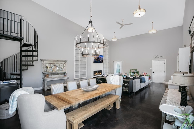 dining space featuring a high ceiling, a large fireplace, and ceiling fan with notable chandelier