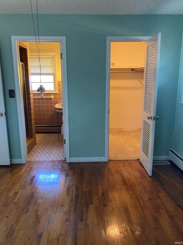 unfurnished bedroom featuring ensuite bath, tile walls, dark hardwood / wood-style flooring, and a closet