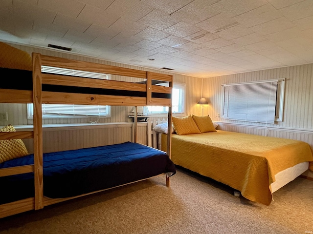 bedroom featuring visible vents, wooden walls, and carpet flooring