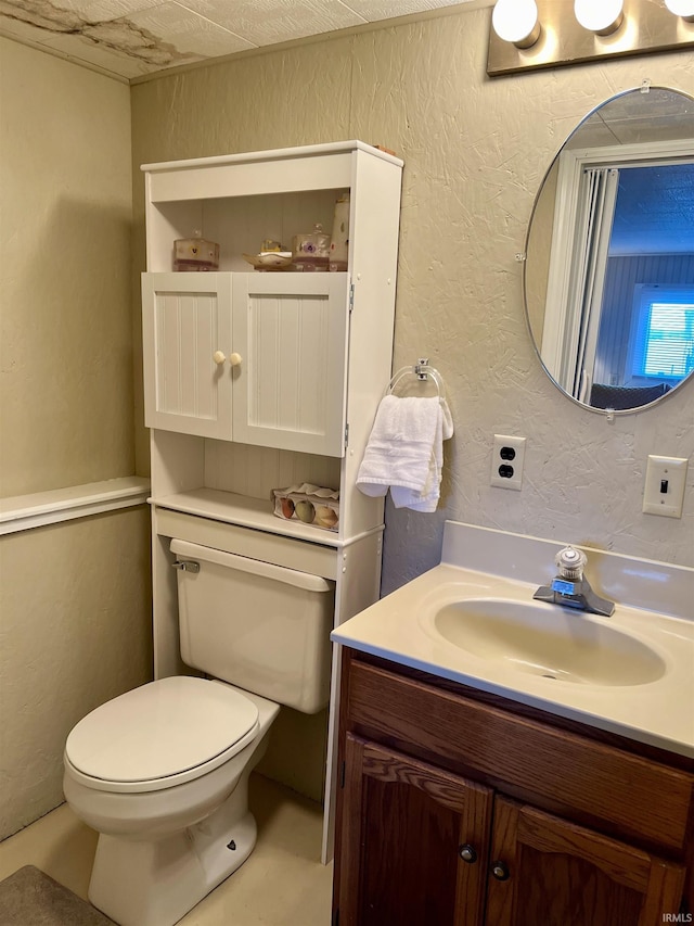 half bathroom with a textured wall, vanity, and toilet