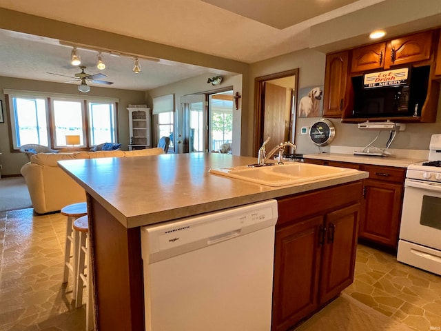 kitchen with a kitchen breakfast bar, white appliances, a center island with sink, sink, and ceiling fan