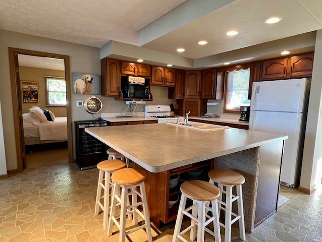 kitchen featuring a breakfast bar area, wine cooler, white appliances, a center island with sink, and sink