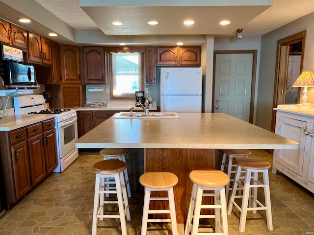 kitchen featuring white appliances, a breakfast bar area, an island with sink, and sink