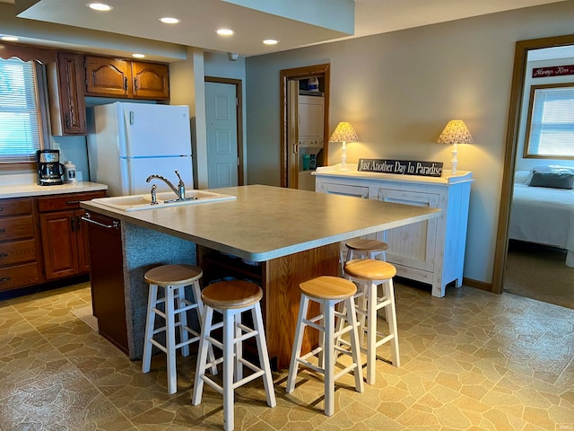 kitchen featuring sink, a center island with sink, white fridge, and a breakfast bar