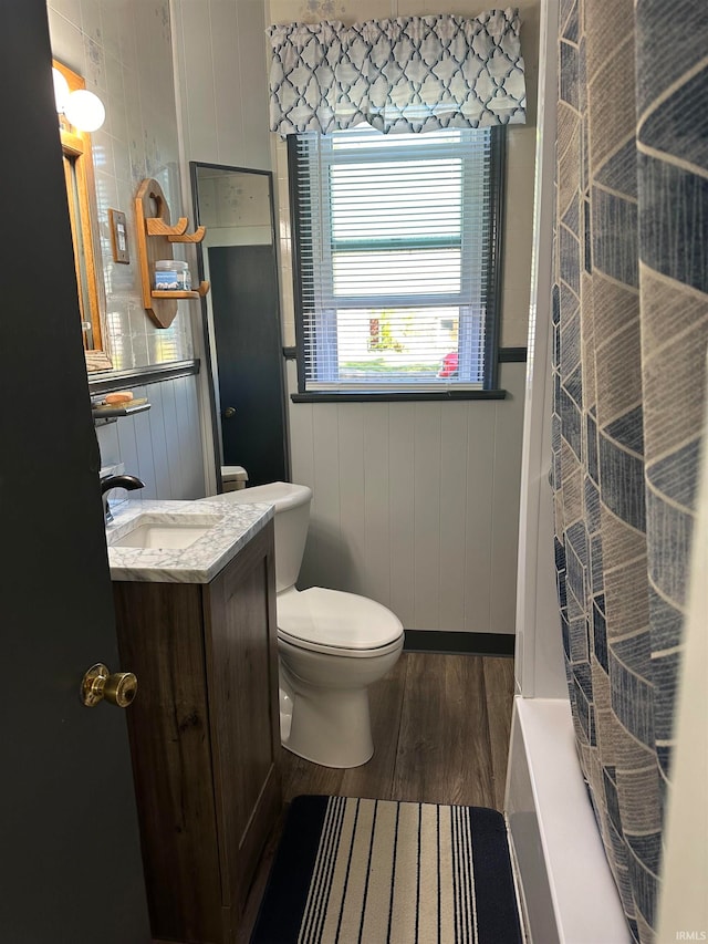 bathroom featuring wooden walls, vanity, hardwood / wood-style flooring, curtained shower, and toilet