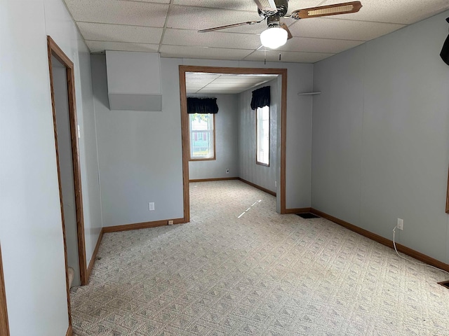 carpeted spare room with ceiling fan and a drop ceiling