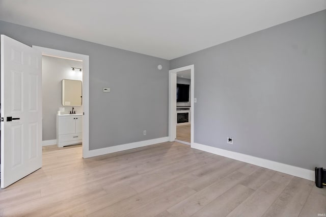 unfurnished bedroom featuring ensuite bathroom, sink, and light hardwood / wood-style floors