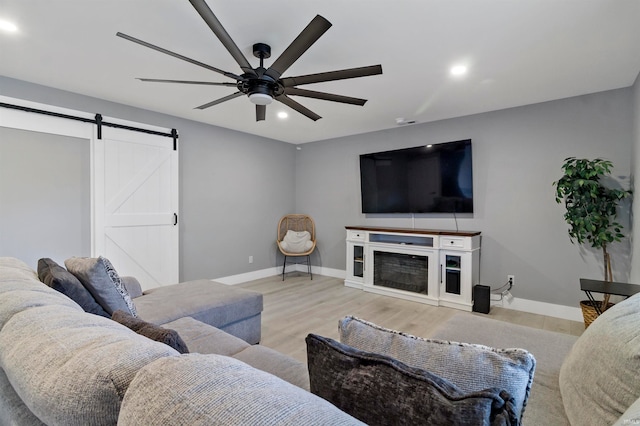 living room with a barn door, ceiling fan, a fireplace, and light hardwood / wood-style flooring