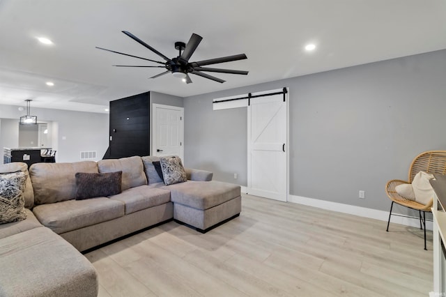 living room with light wood-type flooring, ceiling fan, and a barn door