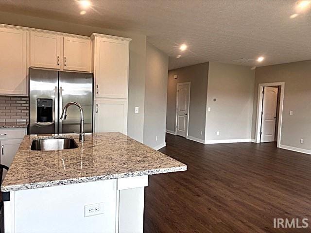 kitchen featuring white cabinets, stainless steel fridge, and an island with sink