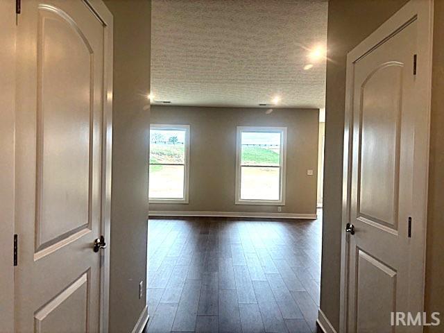 corridor with dark wood-type flooring, baseboards, and a textured ceiling