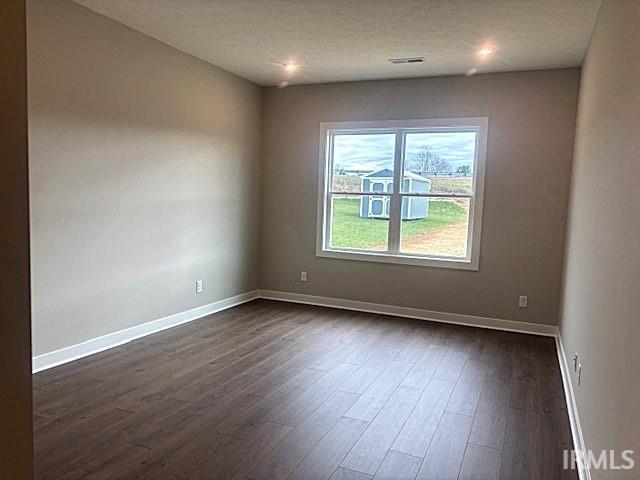 unfurnished room featuring visible vents, baseboards, a textured ceiling, and dark wood finished floors