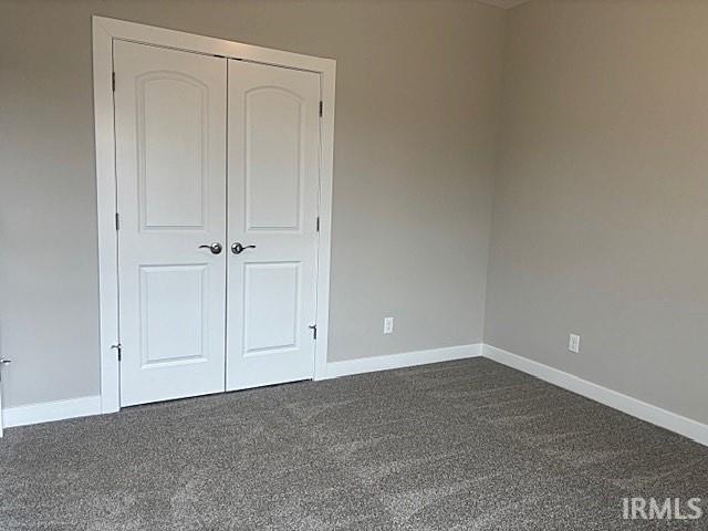 unfurnished bedroom featuring a closet, dark carpet, and baseboards