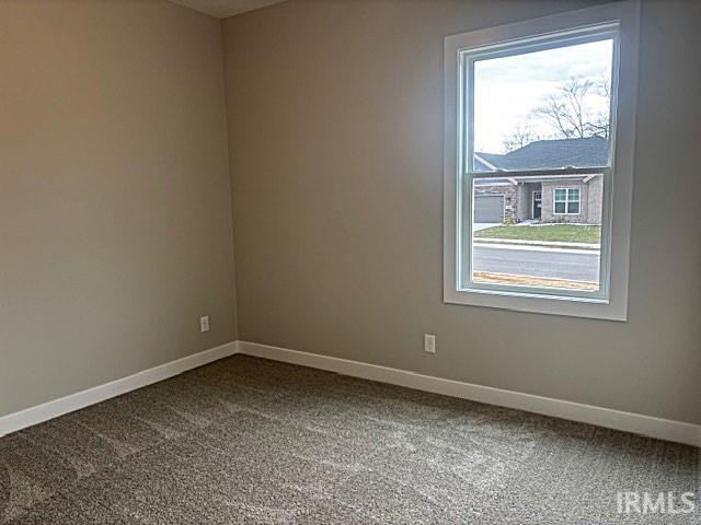 spare room featuring plenty of natural light, baseboards, and dark carpet