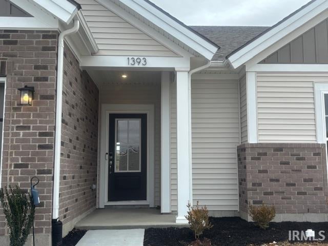 entrance to property with brick siding, board and batten siding, and a shingled roof