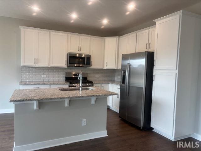 kitchen featuring a sink, white cabinetry, stainless steel appliances, light stone countertops, and dark wood-style flooring