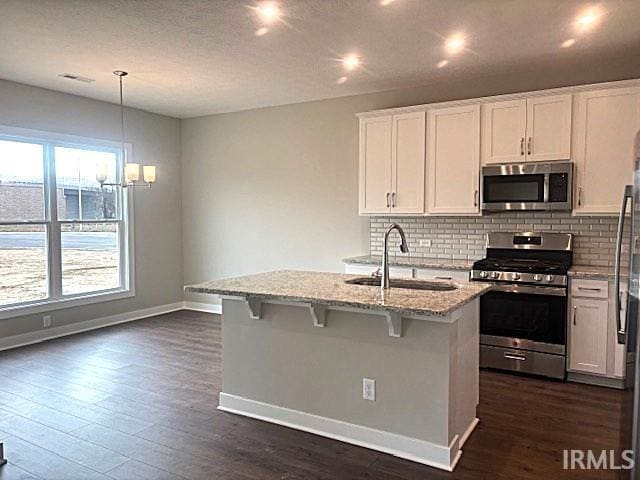 kitchen with light stone countertops, stainless steel appliances, pendant lighting, white cabinets, and an island with sink