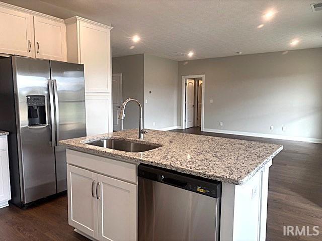 kitchen featuring dark wood finished floors, a kitchen island with sink, a sink, stainless steel appliances, and open floor plan