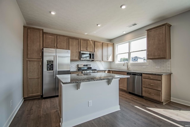 kitchen featuring dark stone countertops, stainless steel appliances, dark wood-type flooring, and a center island