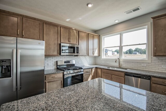 kitchen with decorative backsplash, stone counters, sink, and stainless steel appliances