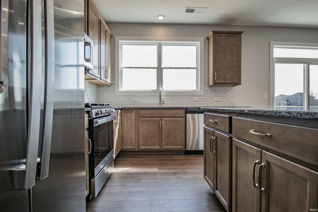 kitchen featuring stainless steel appliances, wood-type flooring, decorative backsplash, and a wealth of natural light