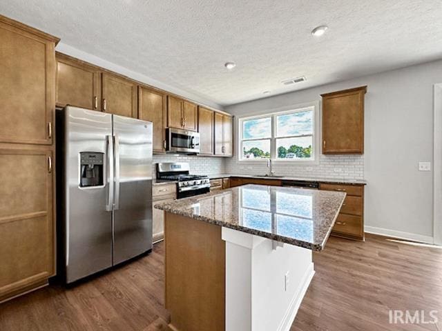 kitchen featuring a kitchen island, stainless steel appliances, tasteful backsplash, dark hardwood / wood-style flooring, and stone countertops