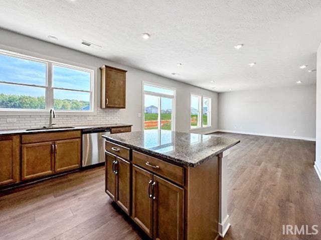 kitchen featuring dark stone countertops, a healthy amount of sunlight, stainless steel dishwasher, and dark hardwood / wood-style floors