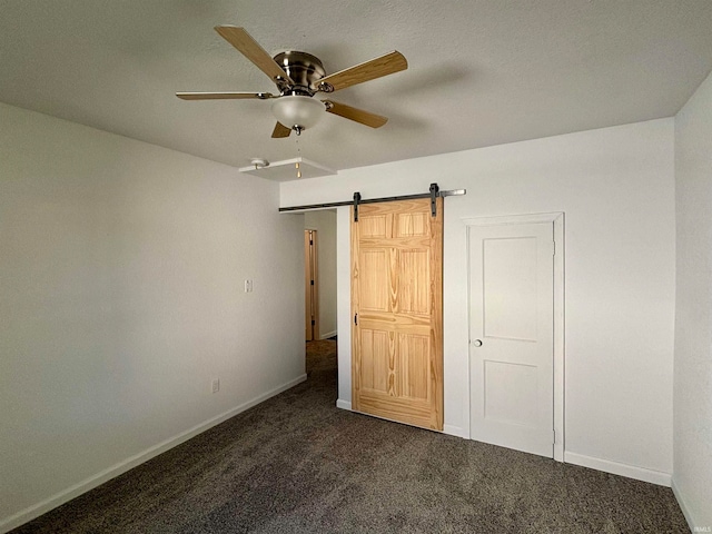 unfurnished bedroom with dark carpet, ceiling fan, and a barn door