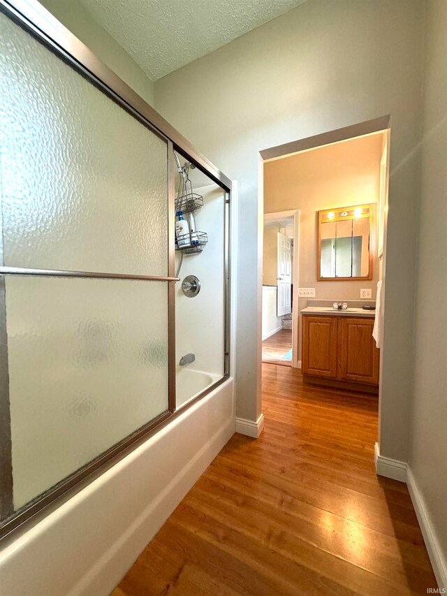 bathroom featuring wood-type flooring, bath / shower combo with glass door, a textured ceiling, and vanity