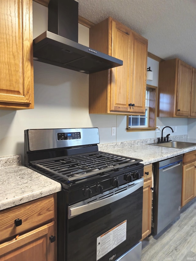 kitchen with a textured ceiling, wall chimney exhaust hood, stainless steel appliances, sink, and light wood-type flooring