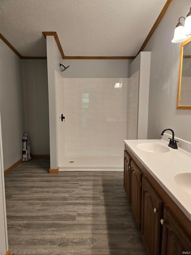 bathroom with a textured ceiling, vanity, a tile shower, crown molding, and hardwood / wood-style flooring