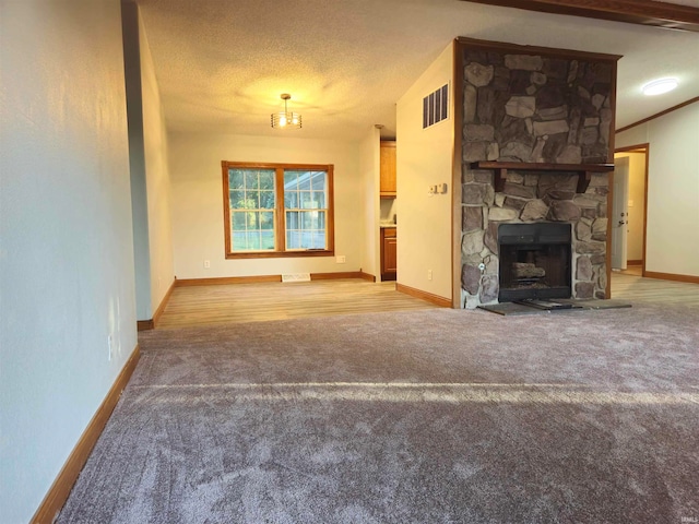 unfurnished living room with a textured ceiling, a stone fireplace, and light wood-type flooring