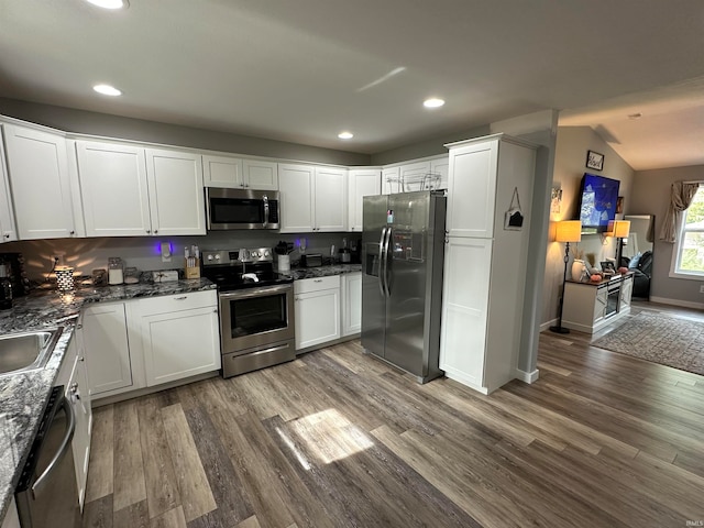 kitchen featuring white cabinets, dark stone countertops, vaulted ceiling, stainless steel appliances, and wood-type flooring