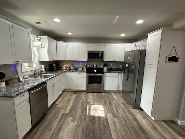 kitchen with hardwood / wood-style flooring, stainless steel appliances, sink, dark stone counters, and pendant lighting