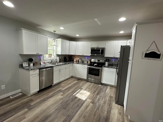 kitchen featuring appliances with stainless steel finishes, hanging light fixtures, sink, hardwood / wood-style flooring, and white cabinets