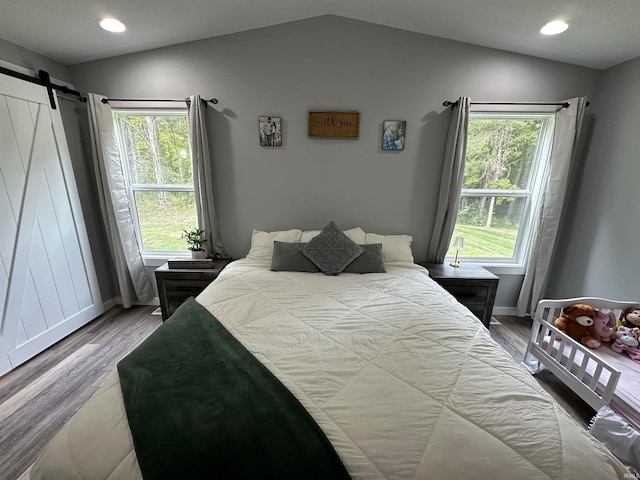 bedroom with a barn door, hardwood / wood-style floors, multiple windows, and vaulted ceiling